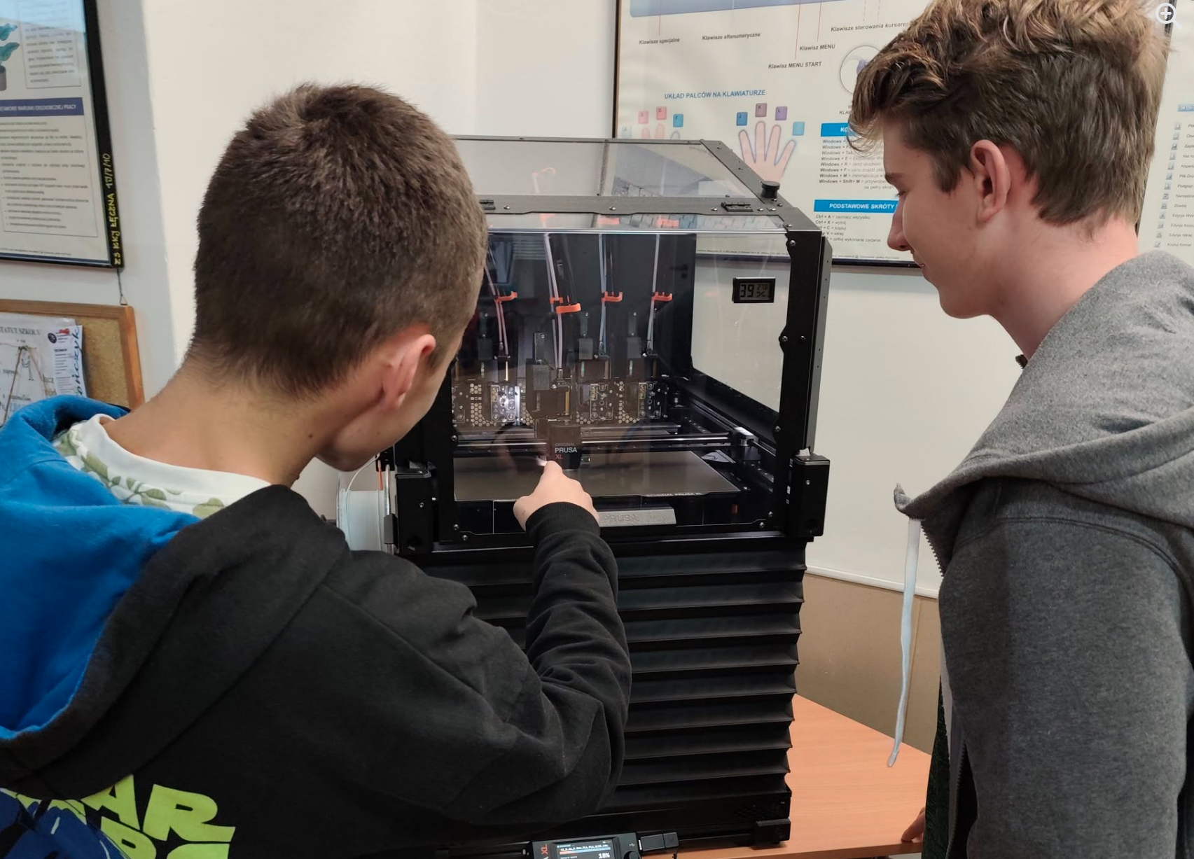 Uczniowie nadzorujący swoje projekty przy drukarce 3D