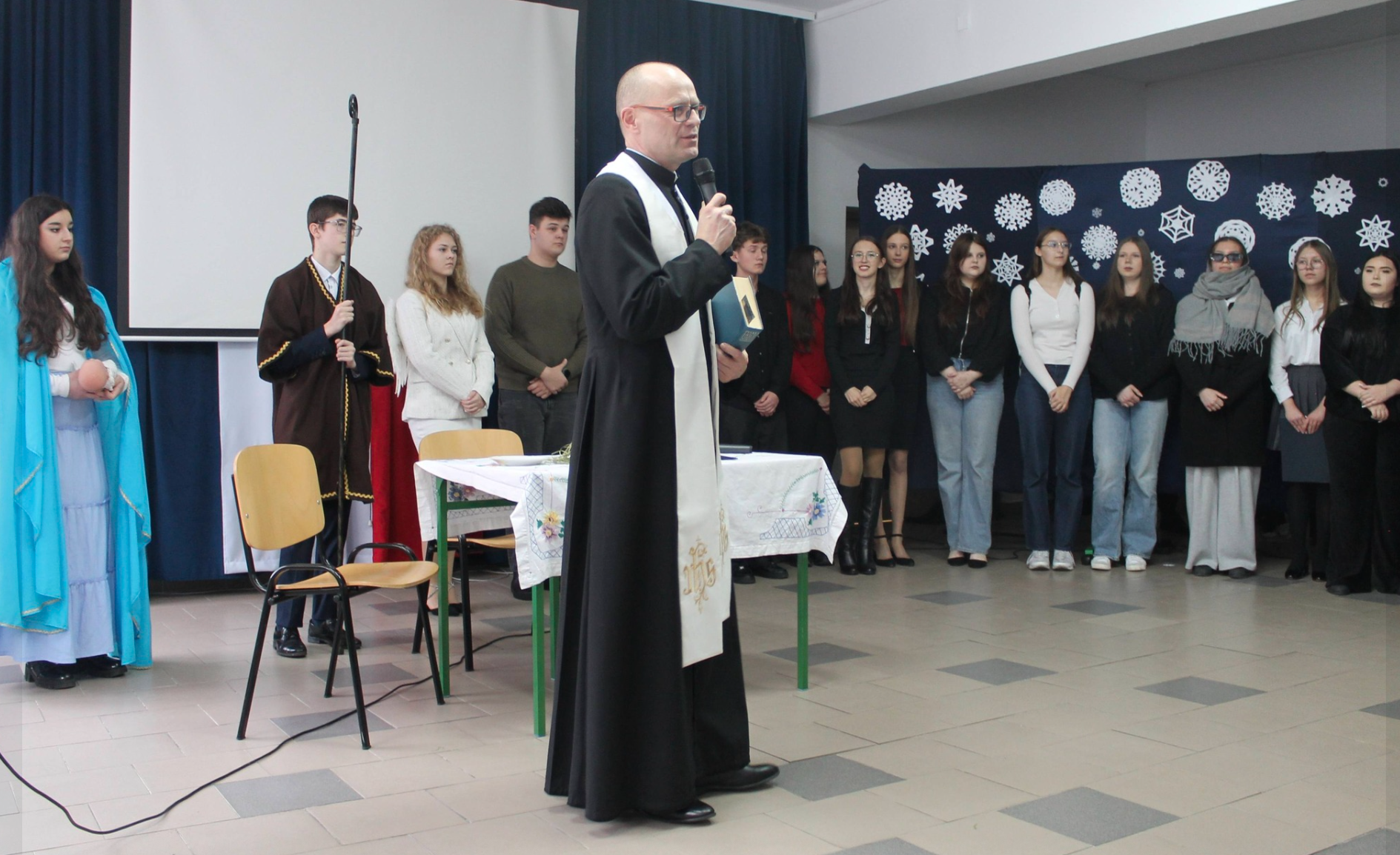 Uczniowie biorący udział w przedstawieniu oraz ksiądz Paweł Kotowski składający życzenia świąteczne społeczności szkolnej